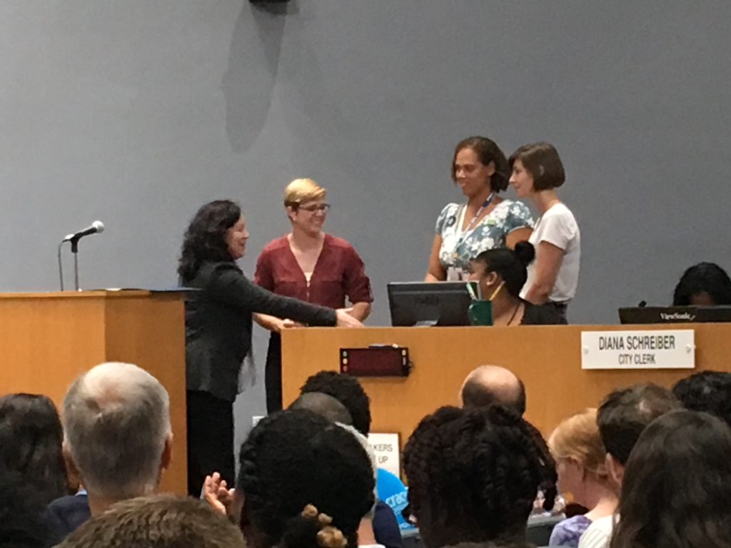 Durham Council Member smiling and facing three representatives of breastfeeding family friendly communities in Durham and presenting the three representatives with the breastfeeding family friendly communities proclamation.